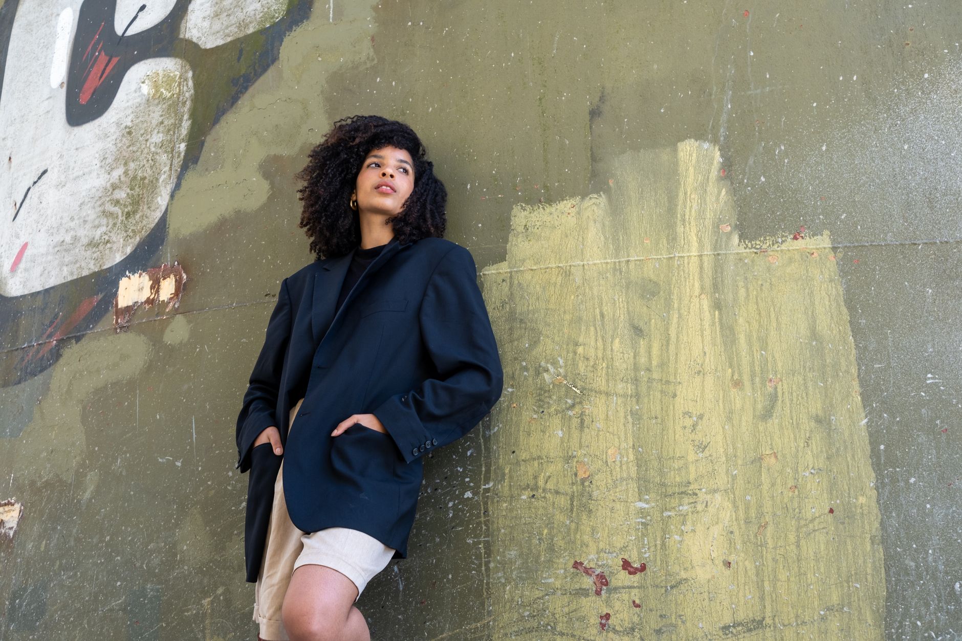 Stylish woman in an oversized blazer leans against a graffiti wall, embodying urban fashion coolness.
