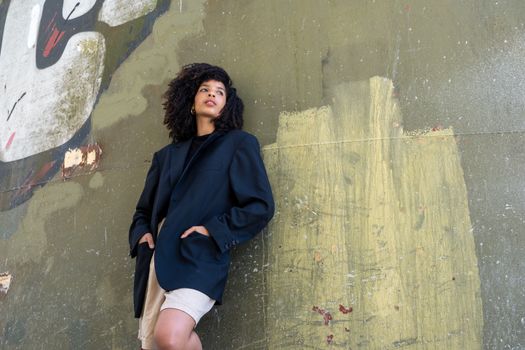 Stylish woman in an oversized blazer leans against a graffiti wall, embodying urban fashion coolness.