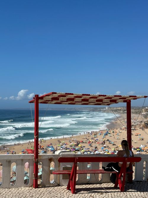 Free Woman sitting on a bench overlooking a lively Silveira beach, Portugal on a sunny summer day. Stock Photo