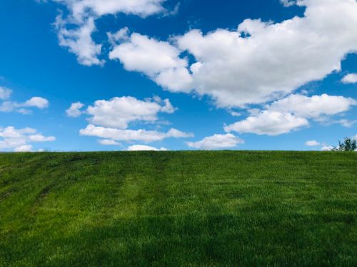 Free Scenic view of a lush green field under a vibrant blue sky with fluffy clouds. Stock Photo