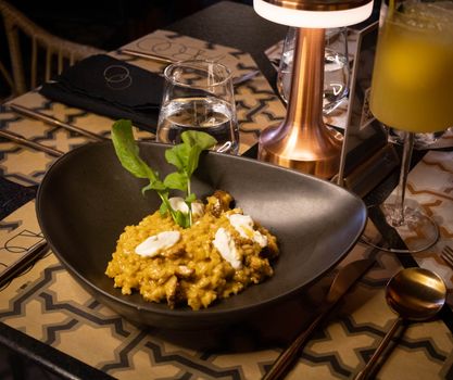 A luxurious bowl of mushroom risotto garnished with arugula served in a stylish restaurant setting.
