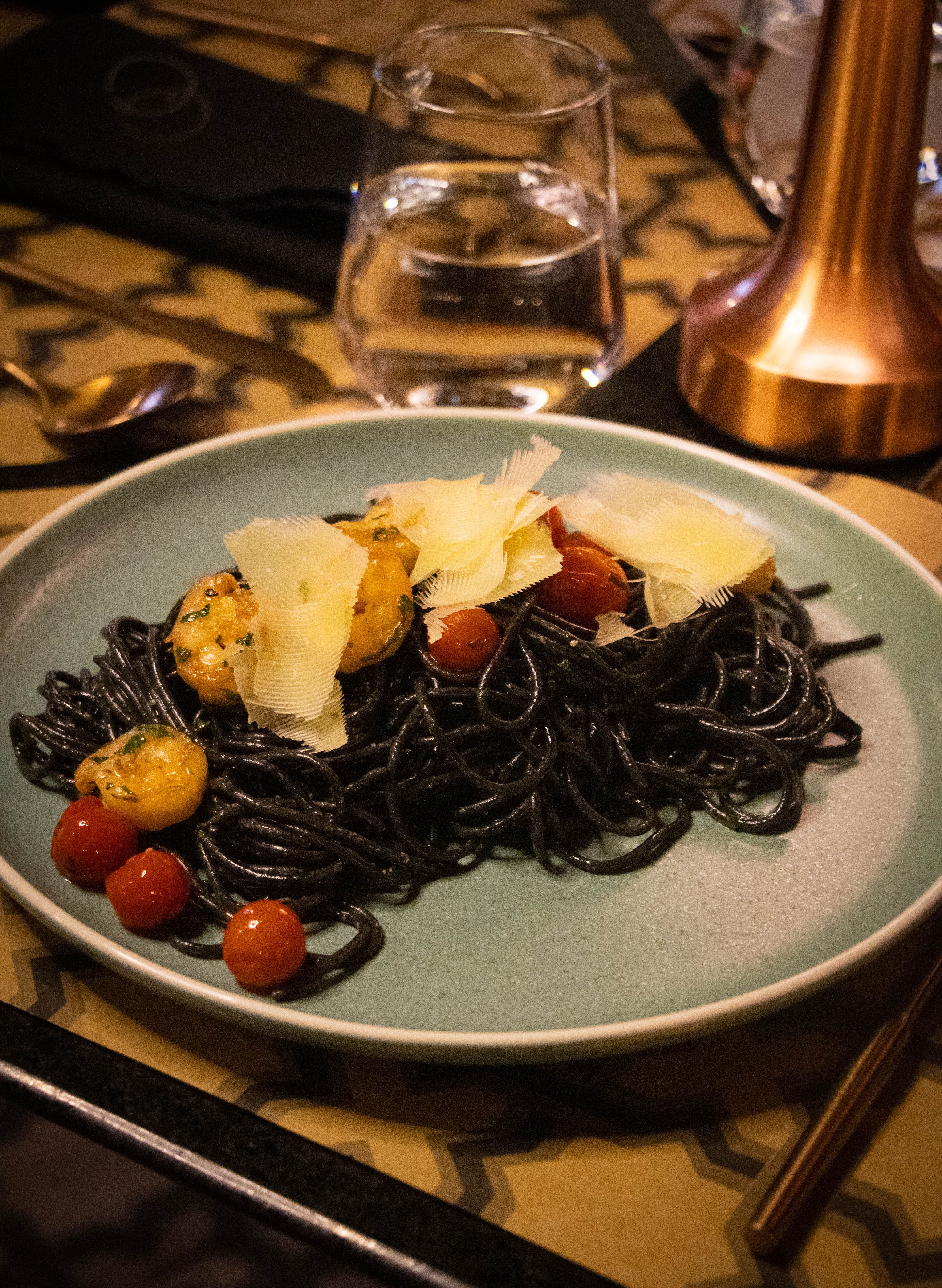 Elegant presentation of black pasta with cherry tomatoes and cheese.
