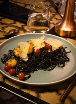 Elegant presentation of black pasta with cherry tomatoes and cheese.