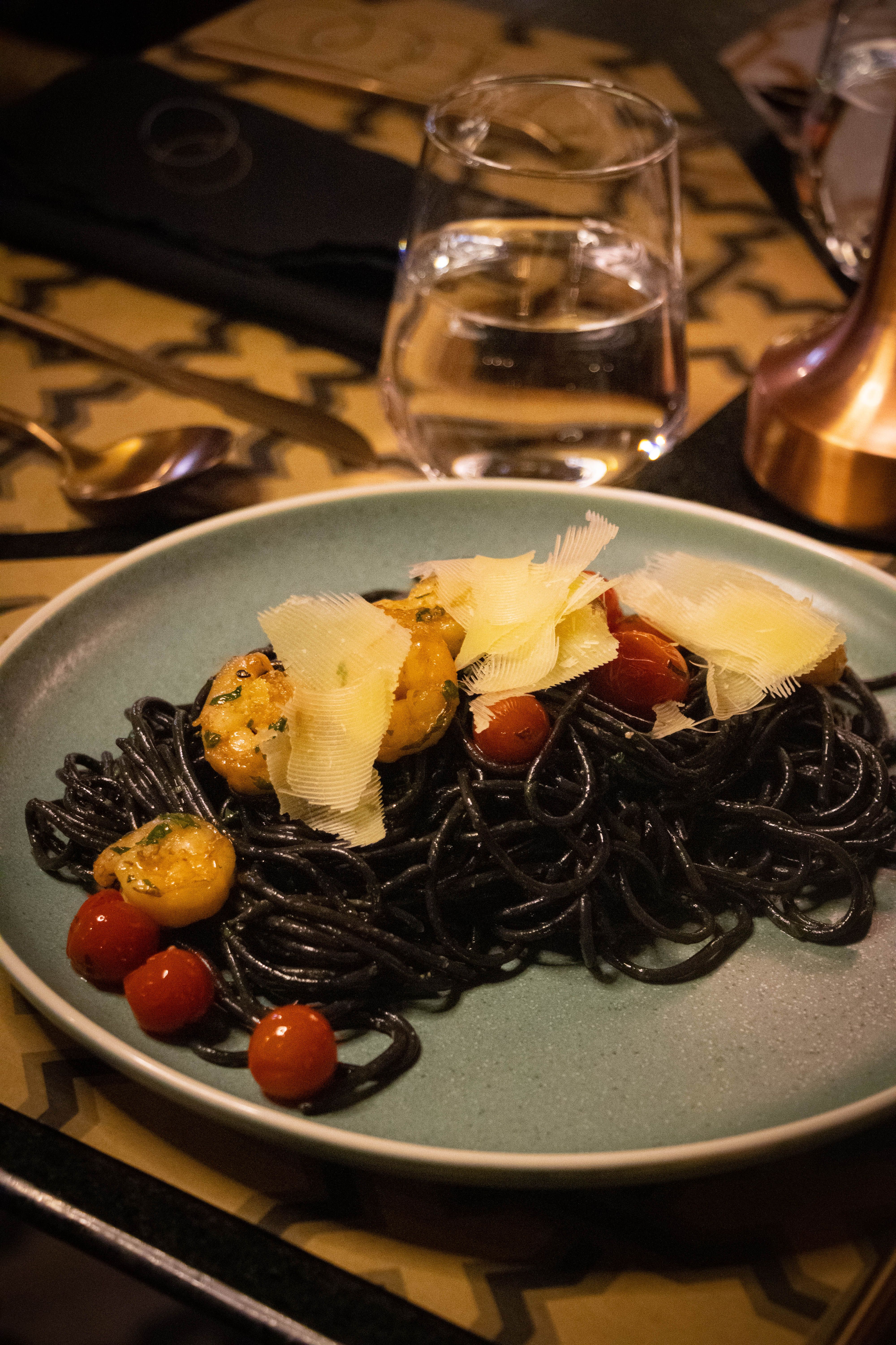 A delicious plate of black pasta with shrimp, cherry tomatoes, and parmesan cheese garnished elegantly.