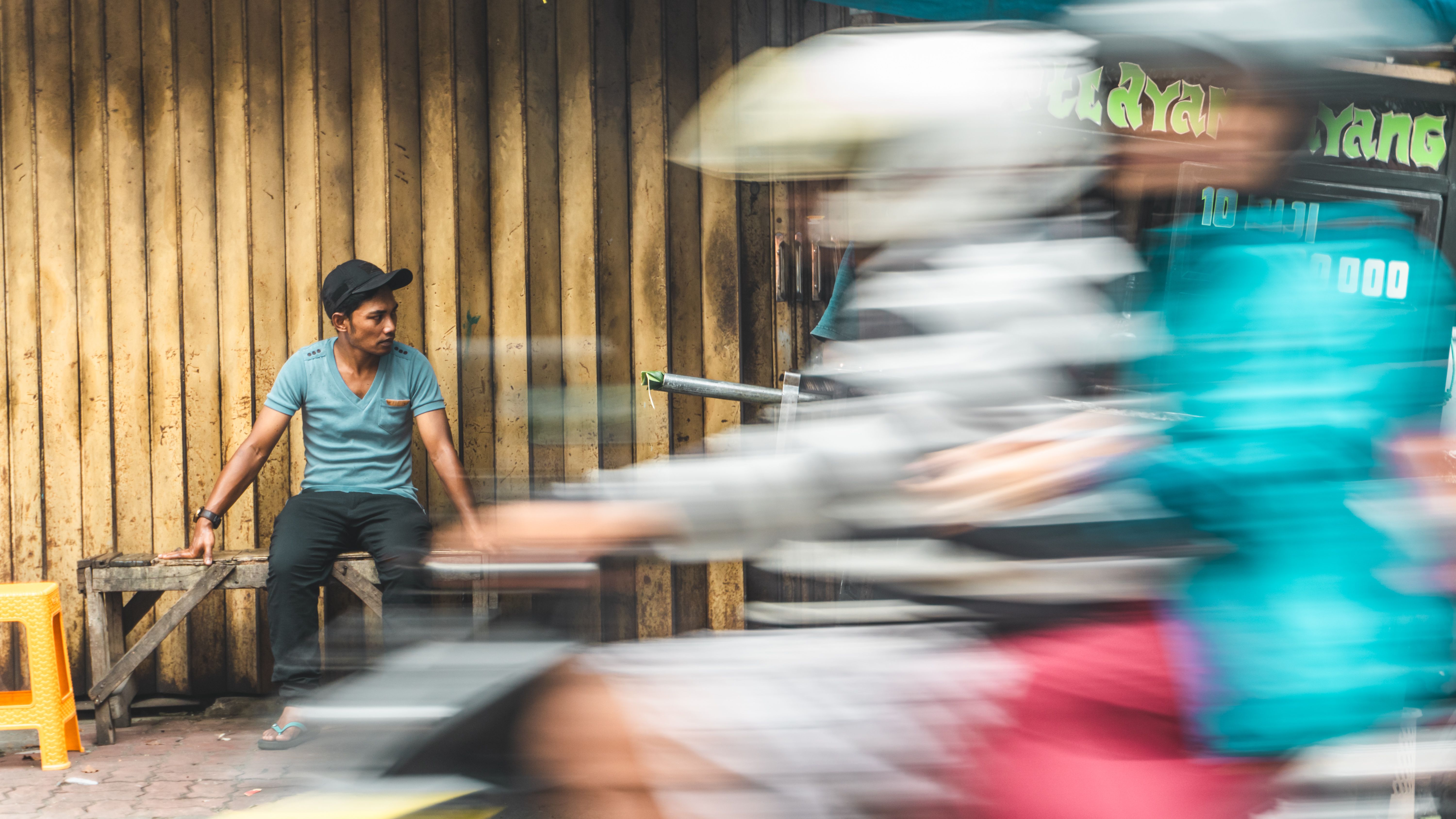 Young Man Sitting on a Bench with Two People Riding a Motor Scooter ...