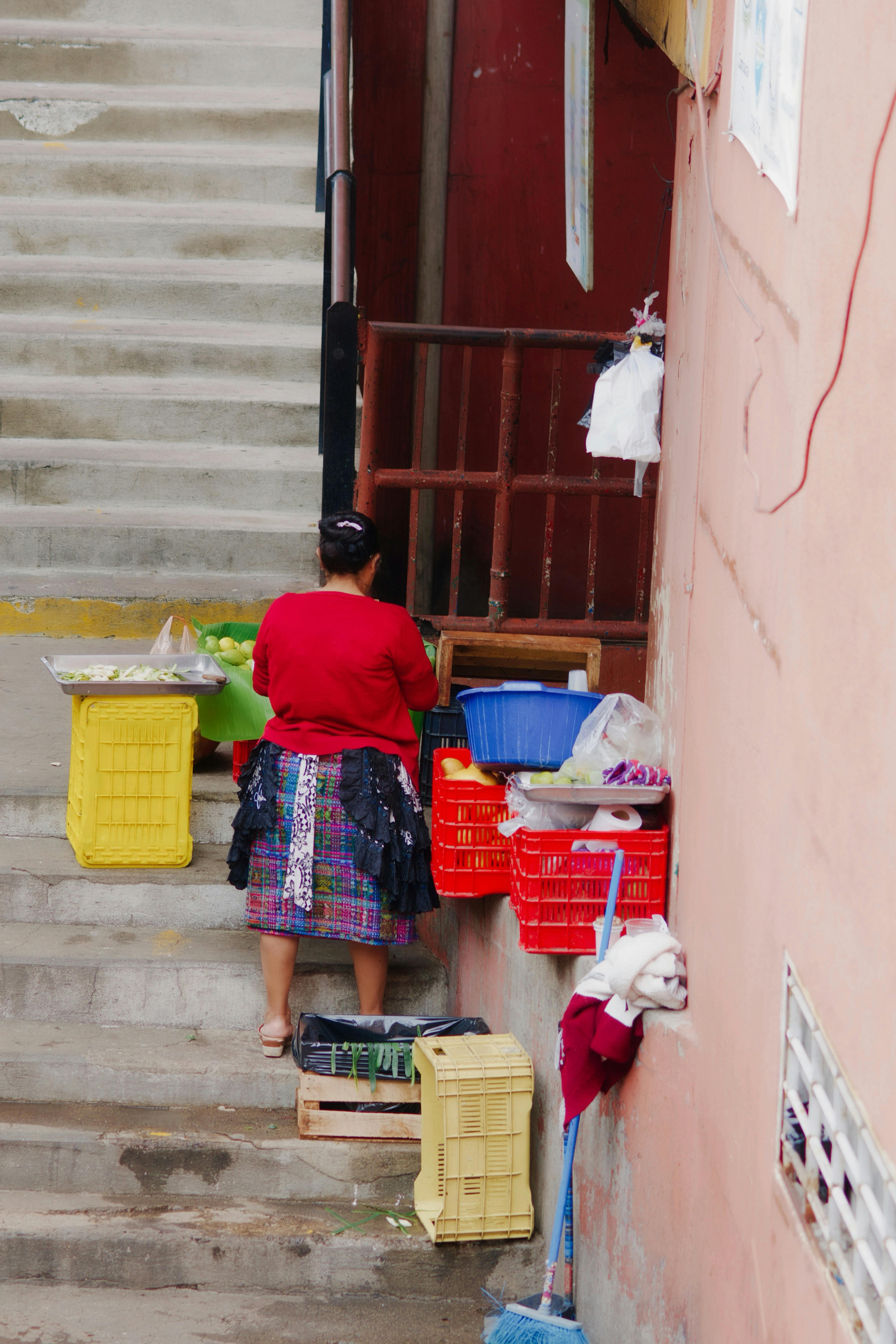 A woman placing colorful baskets on steps in a narrow urban alleyway.
