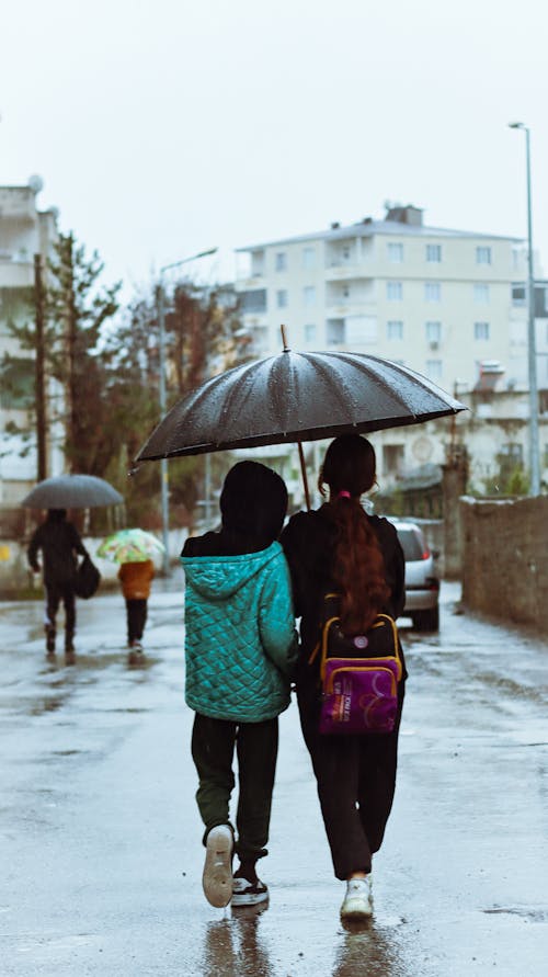 Two people walking down a street with an umbrella