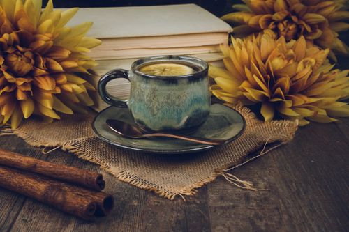 Free Warm tea in an artistic cup surrounded by flowers and books on a rustic table setting. Stock Photo