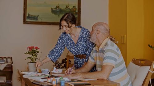 Free An elderly man and a woman enjoy a painting session together at a cozy indoor setting. Stock Photo