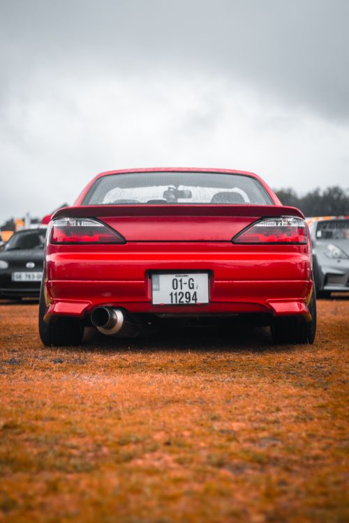 Free Rear view of a bright red sports car parked outdoors with cloudy sky backdrop. Stock Photo