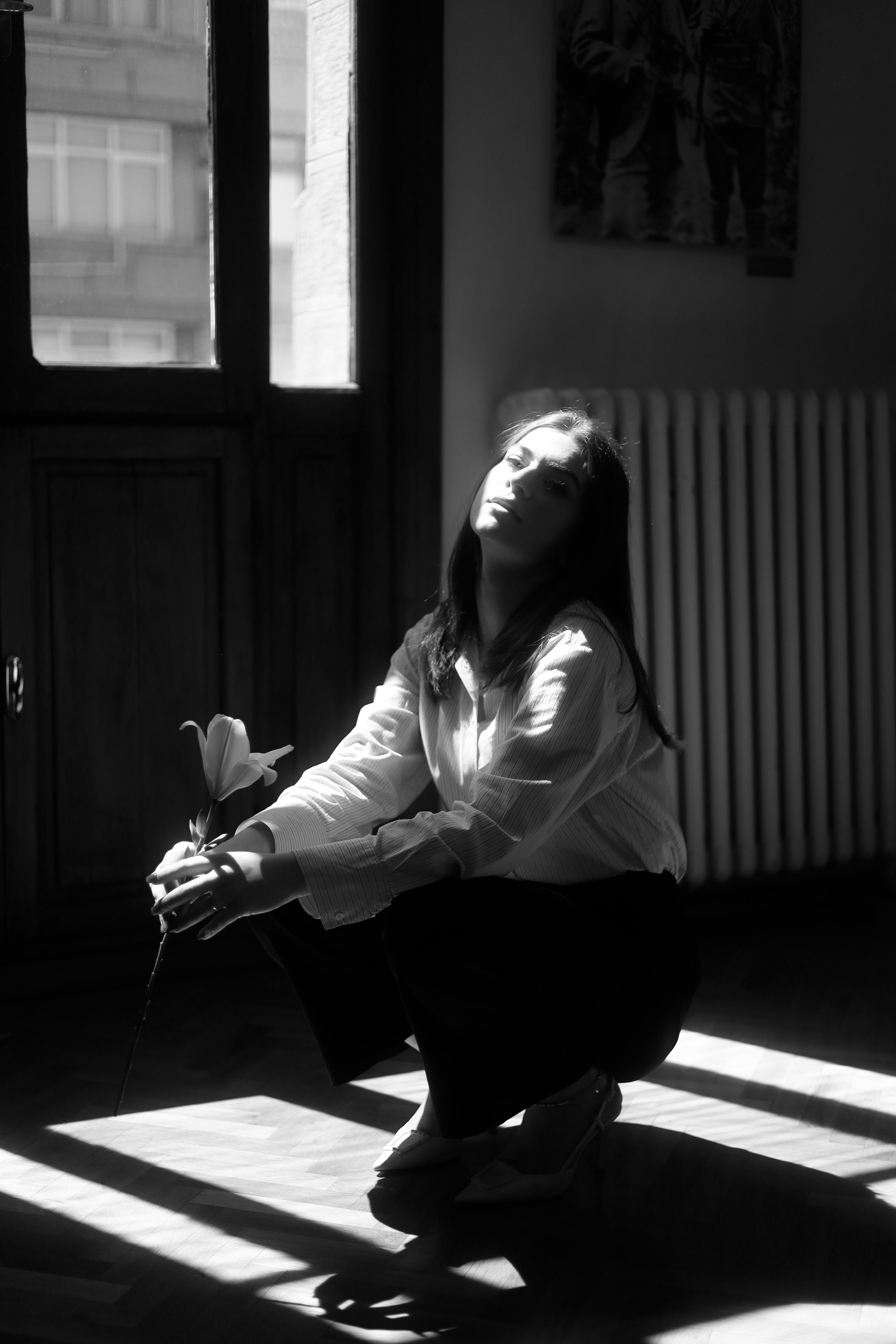 Striking black and white photo of a woman holding a flower in a sunlit room.