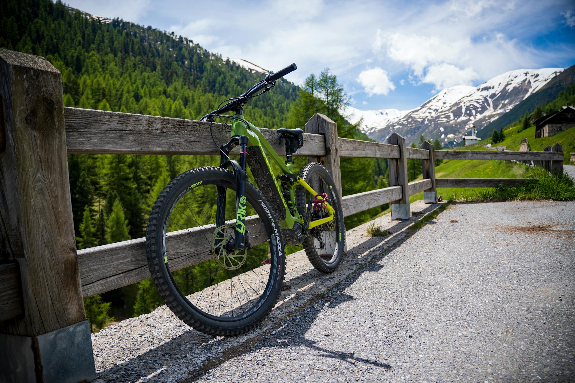 A mountain bike resting against a wooden fence with stunning snowcapped Alps in Livigno, Italy.