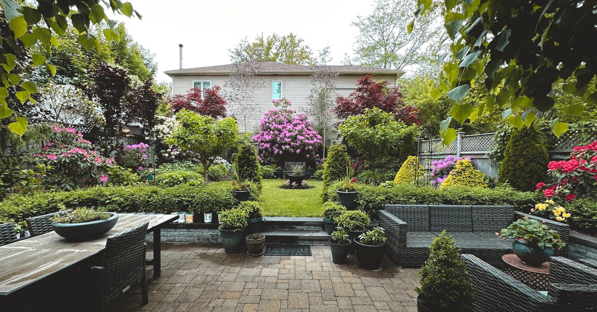 A tranquil backyard garden showcasing vibrant flowers, lush greenery, and patio furniture.