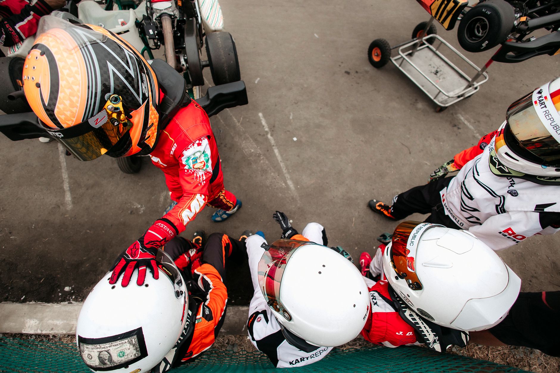 A group of kart racers in racing suits and helmets from above, ready for action.