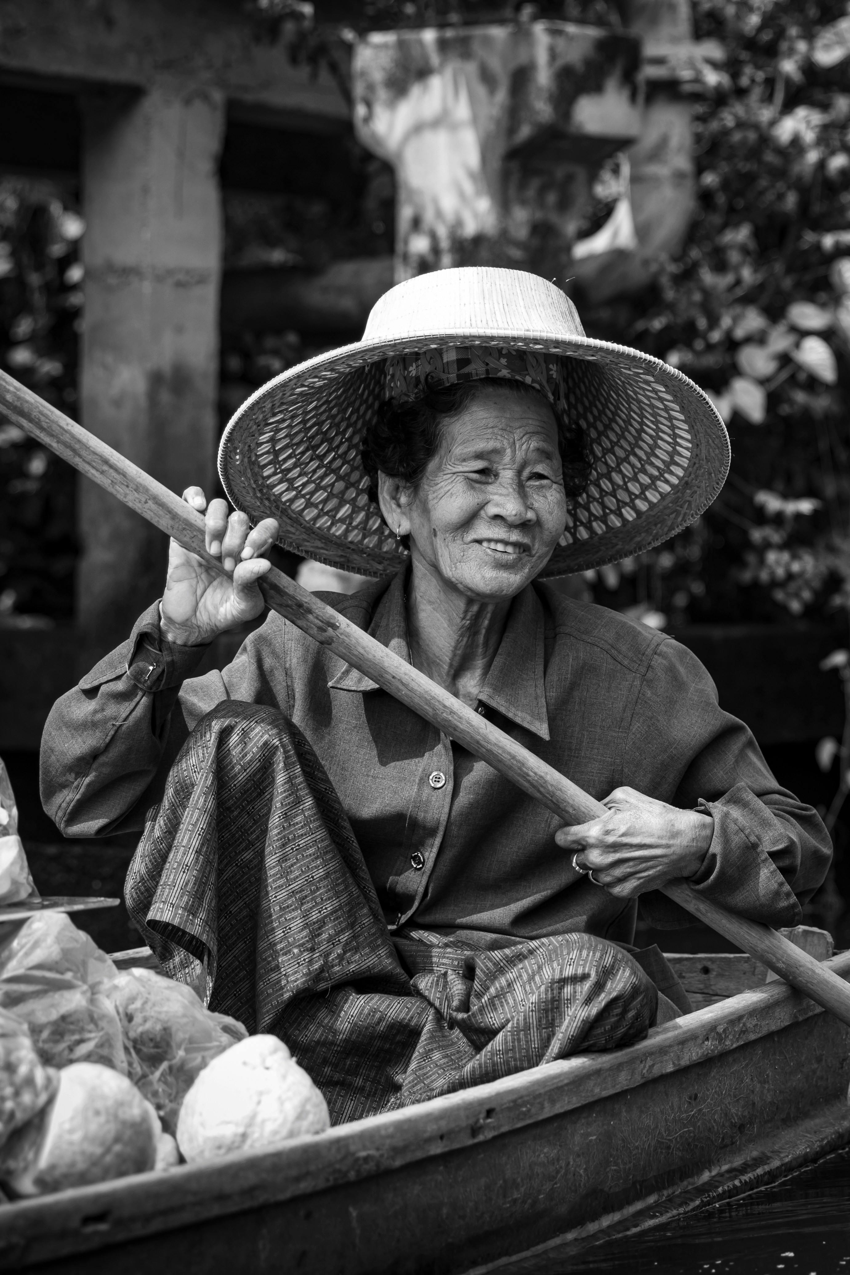 Smiling Asian woman in a boat holding an oar, wearing a hat, in a serene setting.