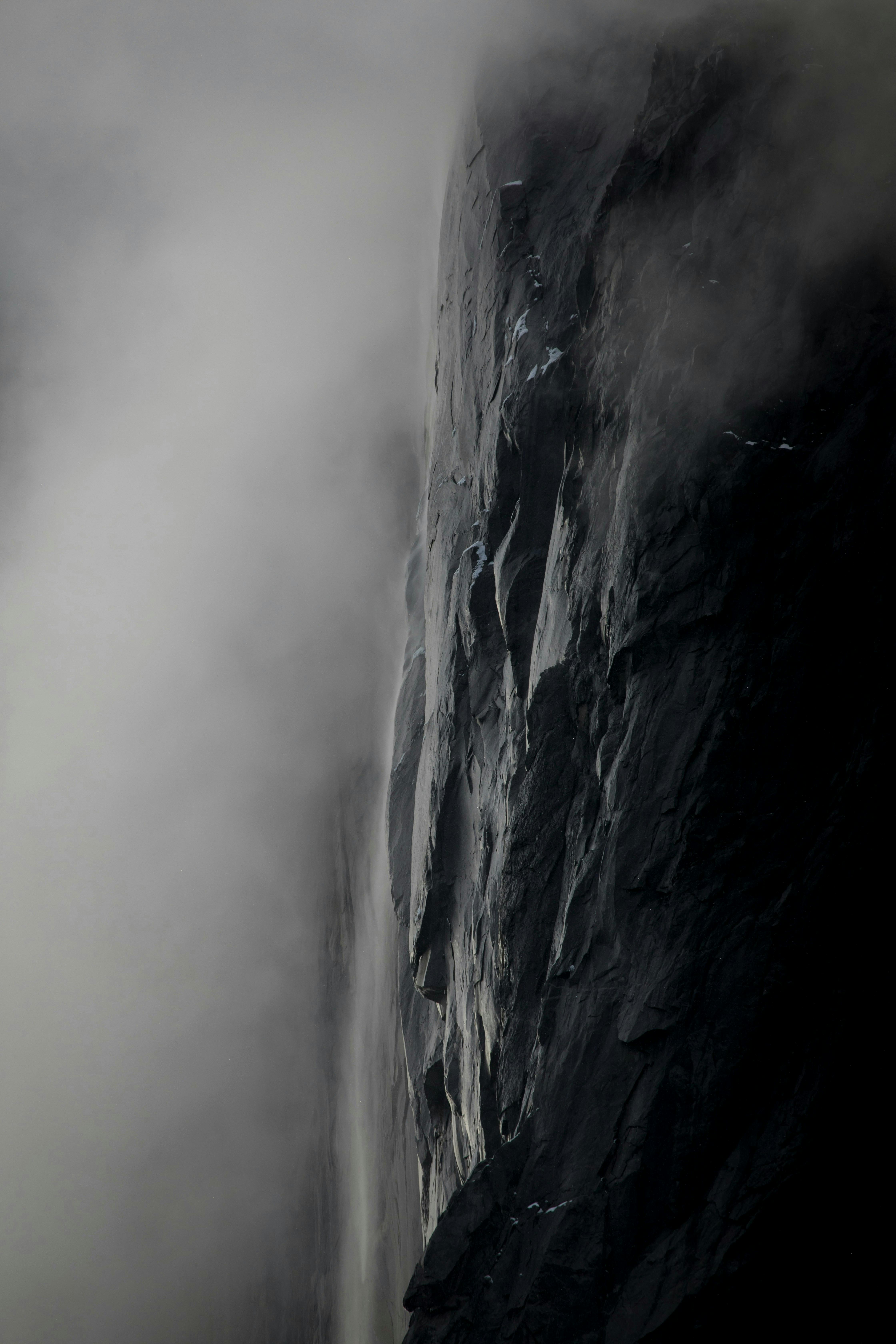 Mysterious and atmospheric cliff shrouded in fog and mist, captured in a vertical shot.