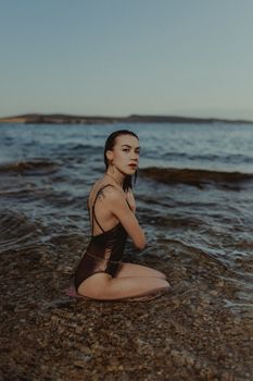 A woman in a swimsuit sits by the calm sea shore during a summer day.