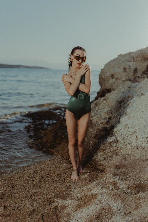 A woman in a green one piece swimsuit standing on the beach