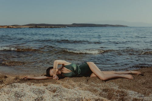 A woman laying on the beach in a green swimsuit