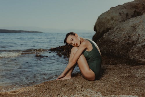 A woman sitting on the beach in a green one piece swimsuit