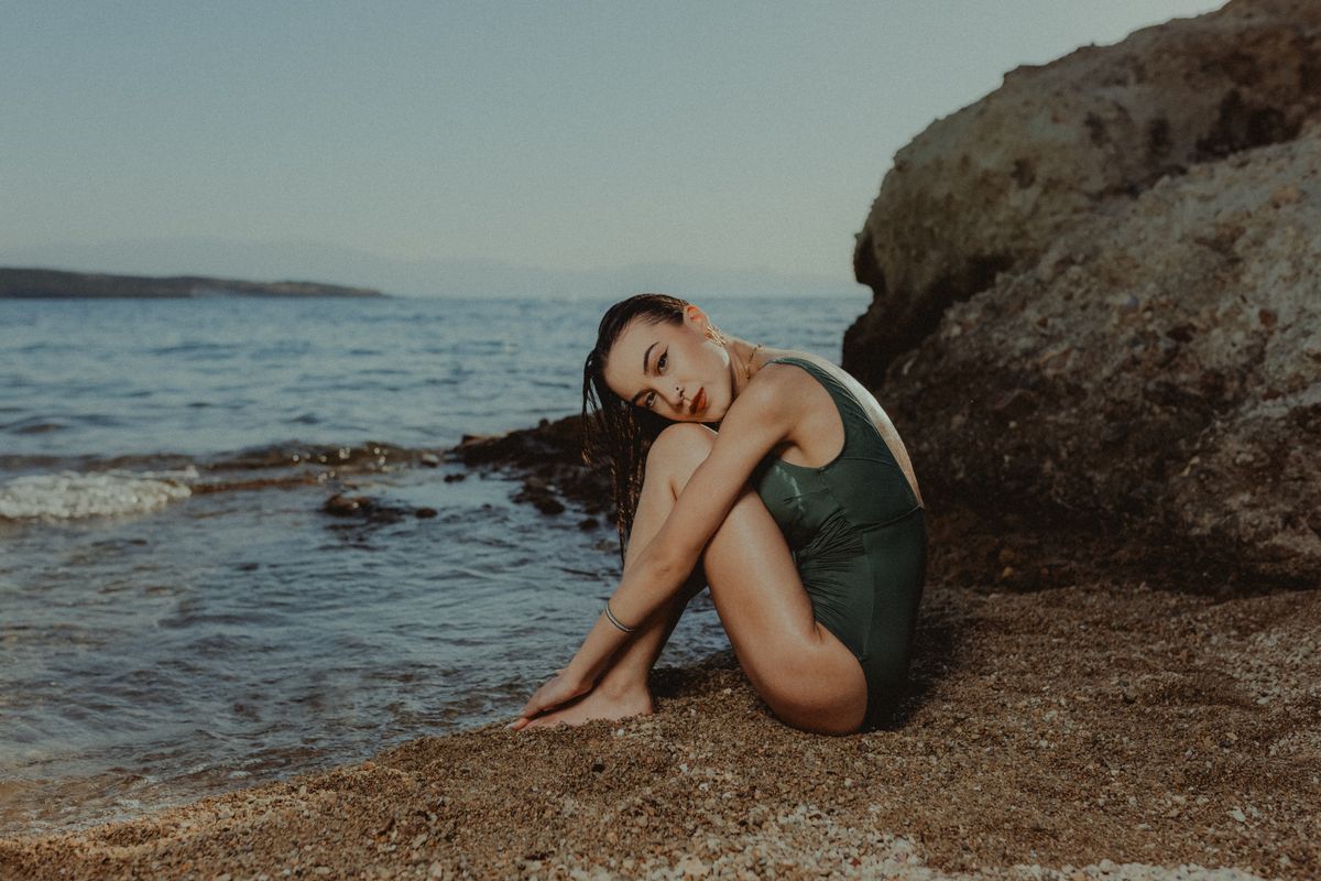 Charming female in swimsuit sitting on sandy beach · Free Stock Photo