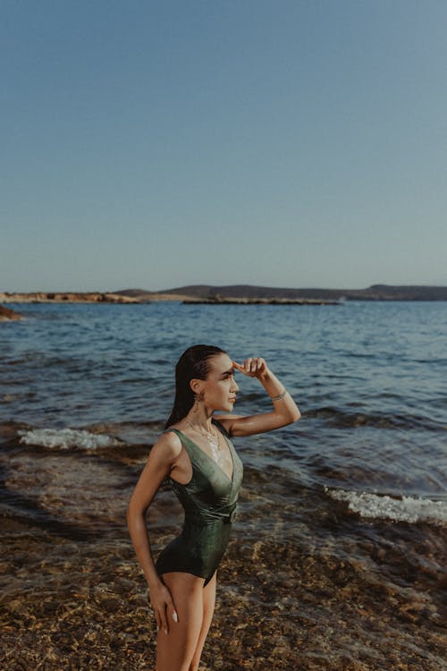 A woman in a green one piece swimsuit standing on the shore