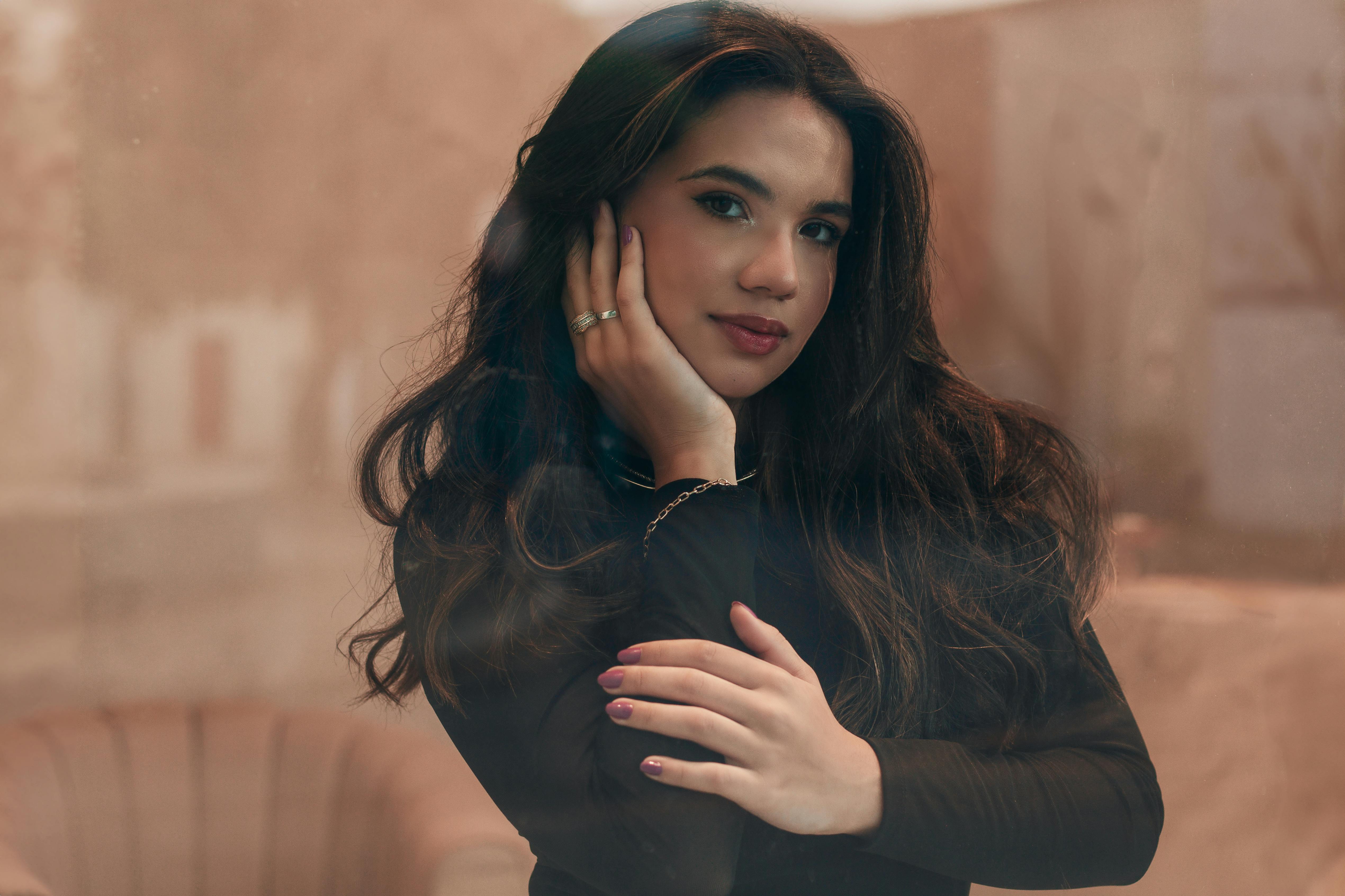 Beautiful portrait of an elegant woman with black hair and a black outfit against a cream background.