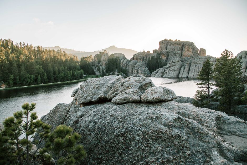 Idyllic landscape with calm waters, rugged rock formations, and lush forest.