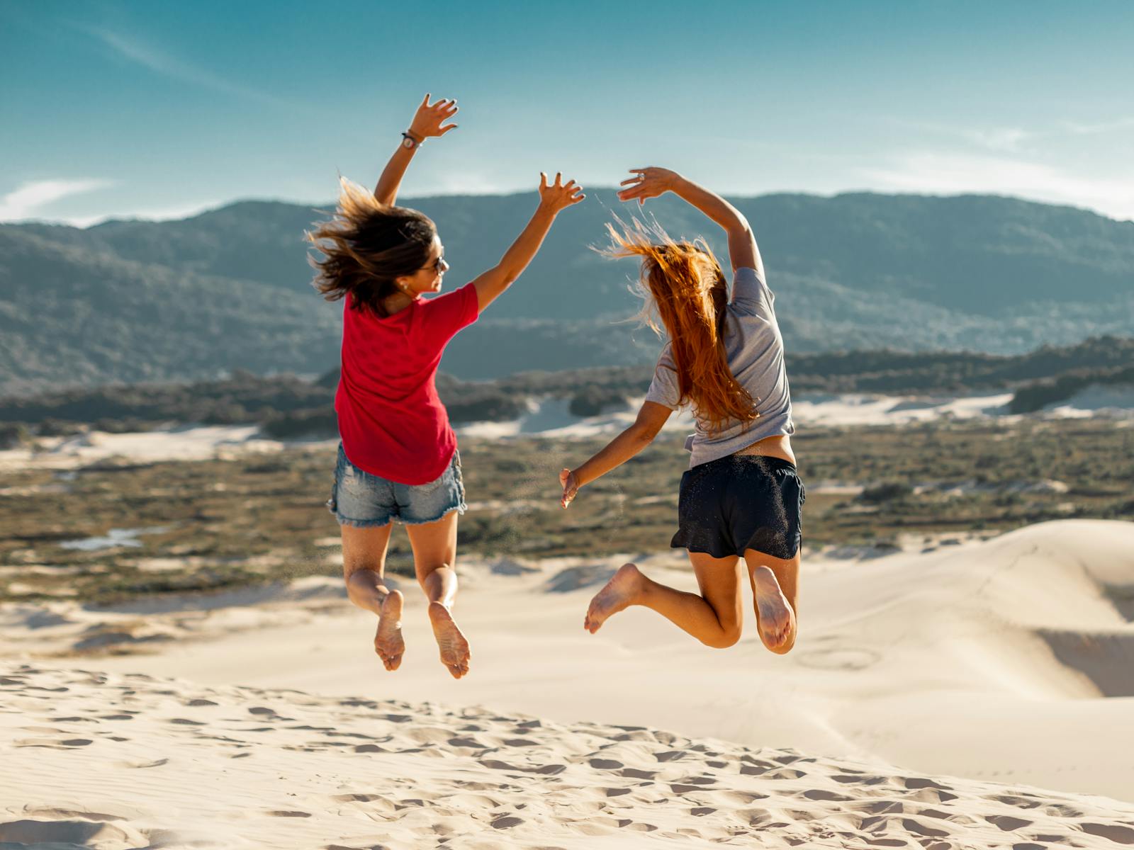Two friends jumping up together on the sand.