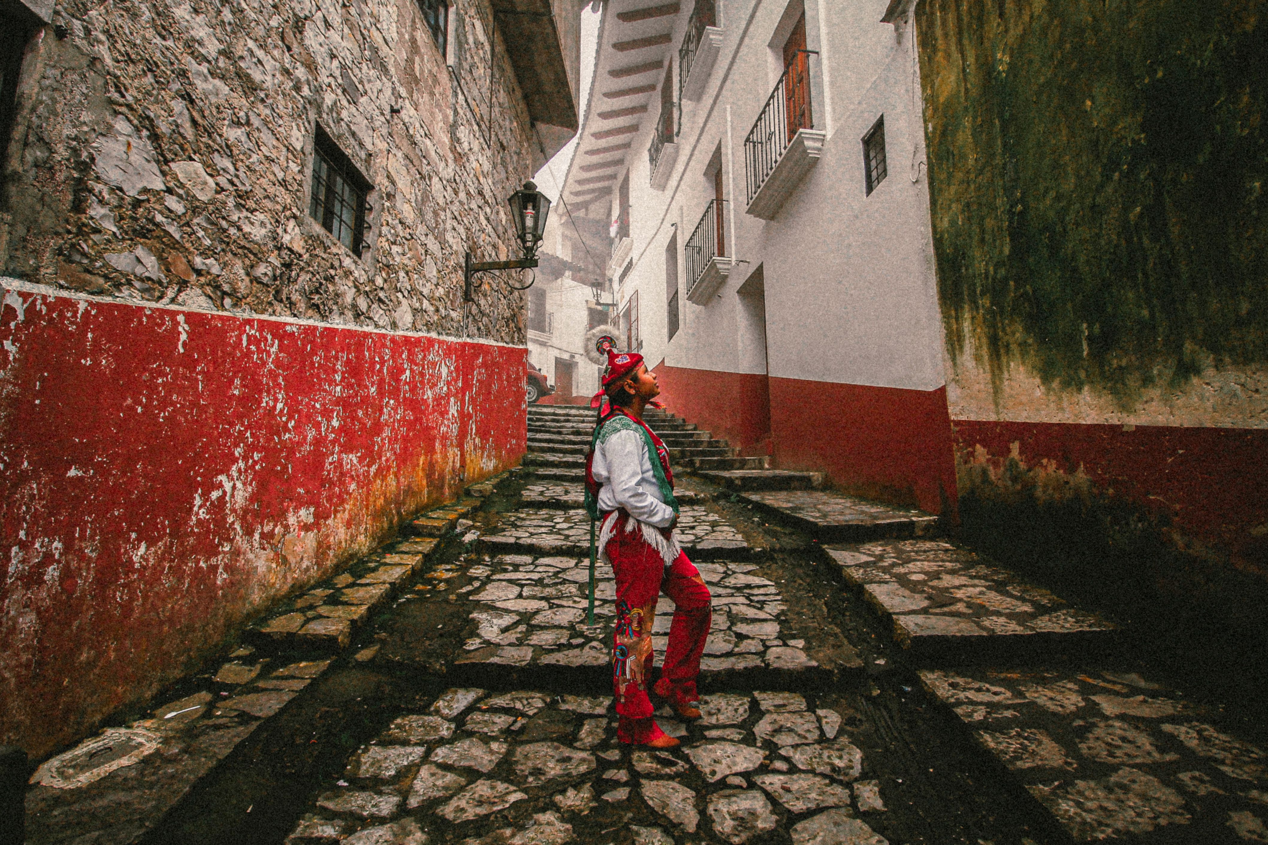 Man in traditional costume stands in a historic alley of Cuetzalan, Puebla, Mexico.
