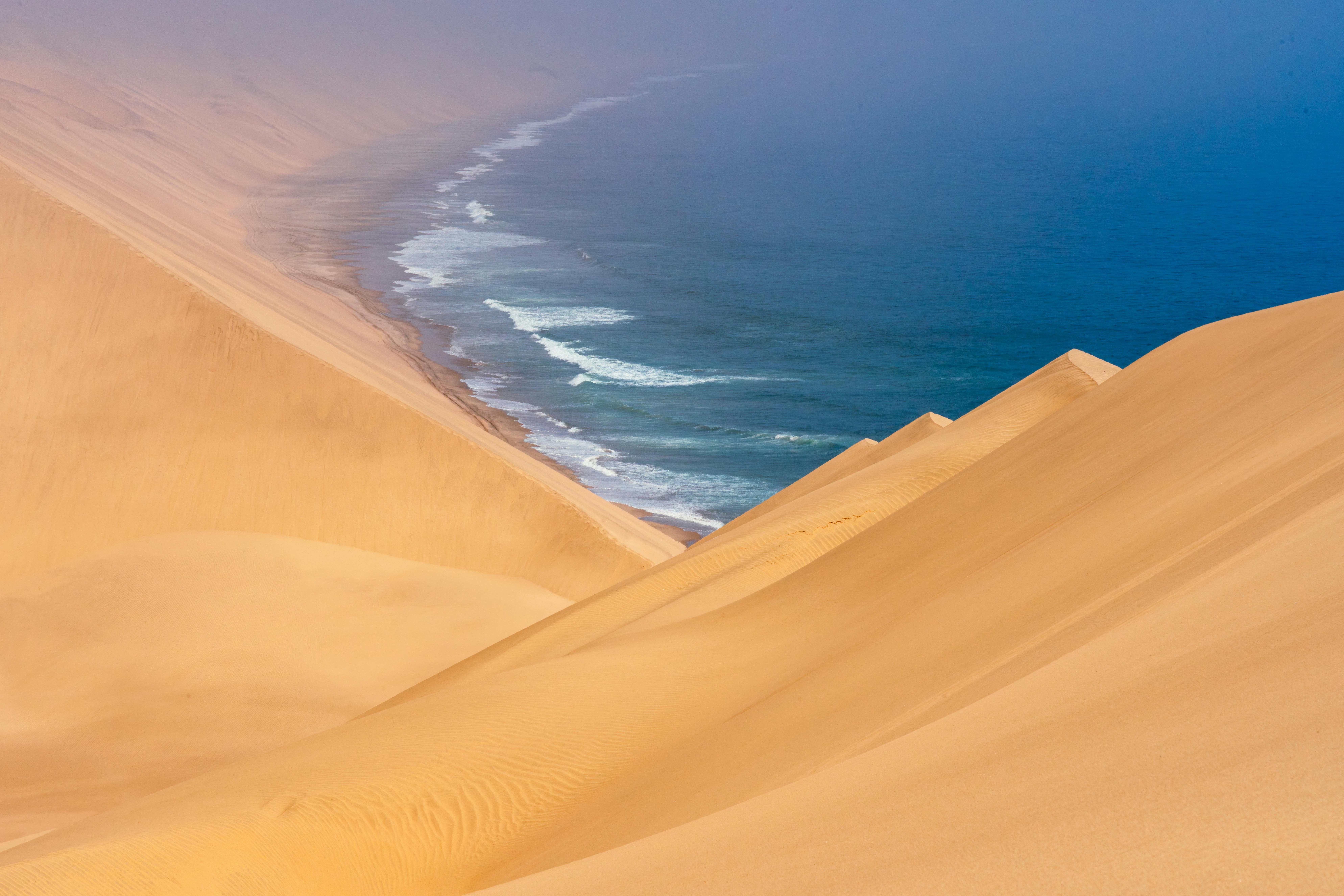A breathtaking view of vast sand dunes merging with the ocean waves at a remote coastline.