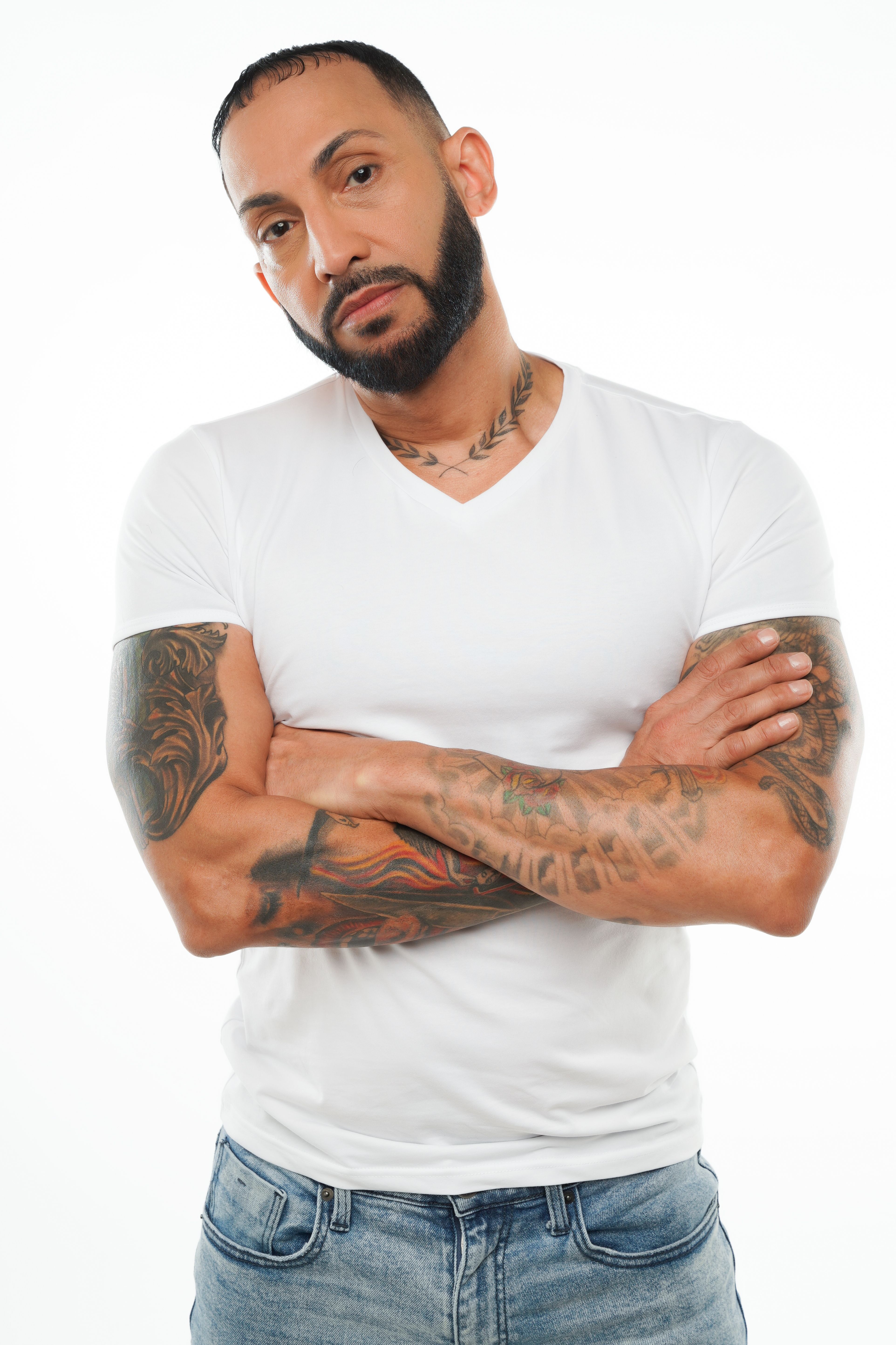 Studio portrait of an adult man with tattoos and beard standing with arms crossed.
