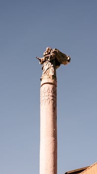 A classic statue atop a column against a clear blue sky in Curitiba, Brazil.