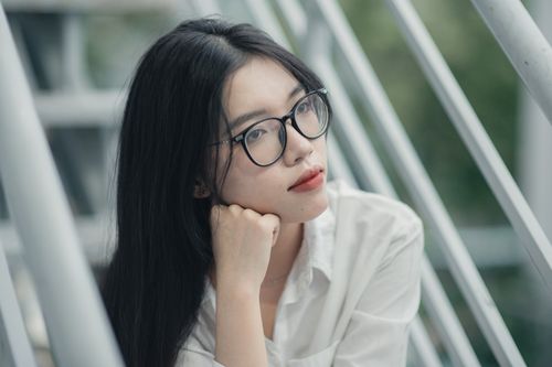 Free Portrait of a young Asian woman wearing eyeglasses, gazing thoughtfully, dressed in white shirt, outdoors. Stock Photo