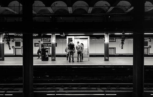 Black and white of anonymous people waiting for train on platform of subway station