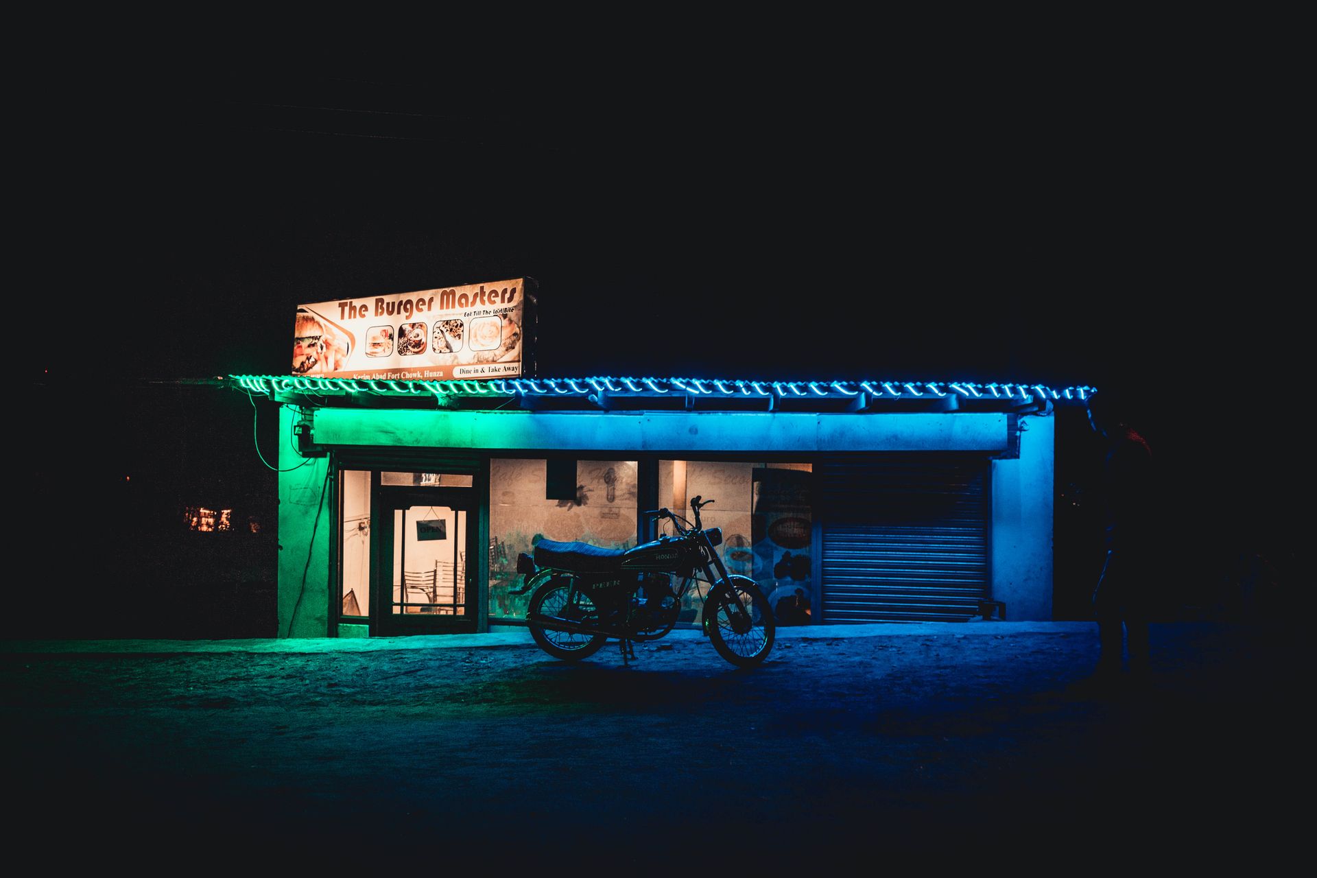 A motorcycle parked outside a neon-lit burger shop at night, with vibrant colors.