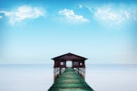 在明亮的蓝天下，平静的大海上，码头通向一座小屋，构成宁静的场景