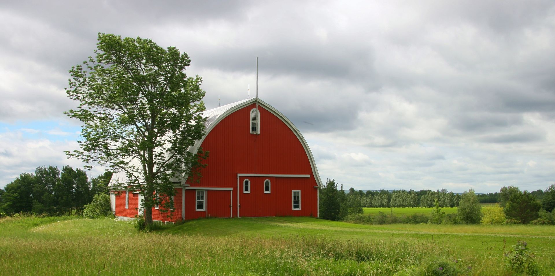A picturesque red barn located on a lush green farm with cloudy skies enhancing the rural landscape.
