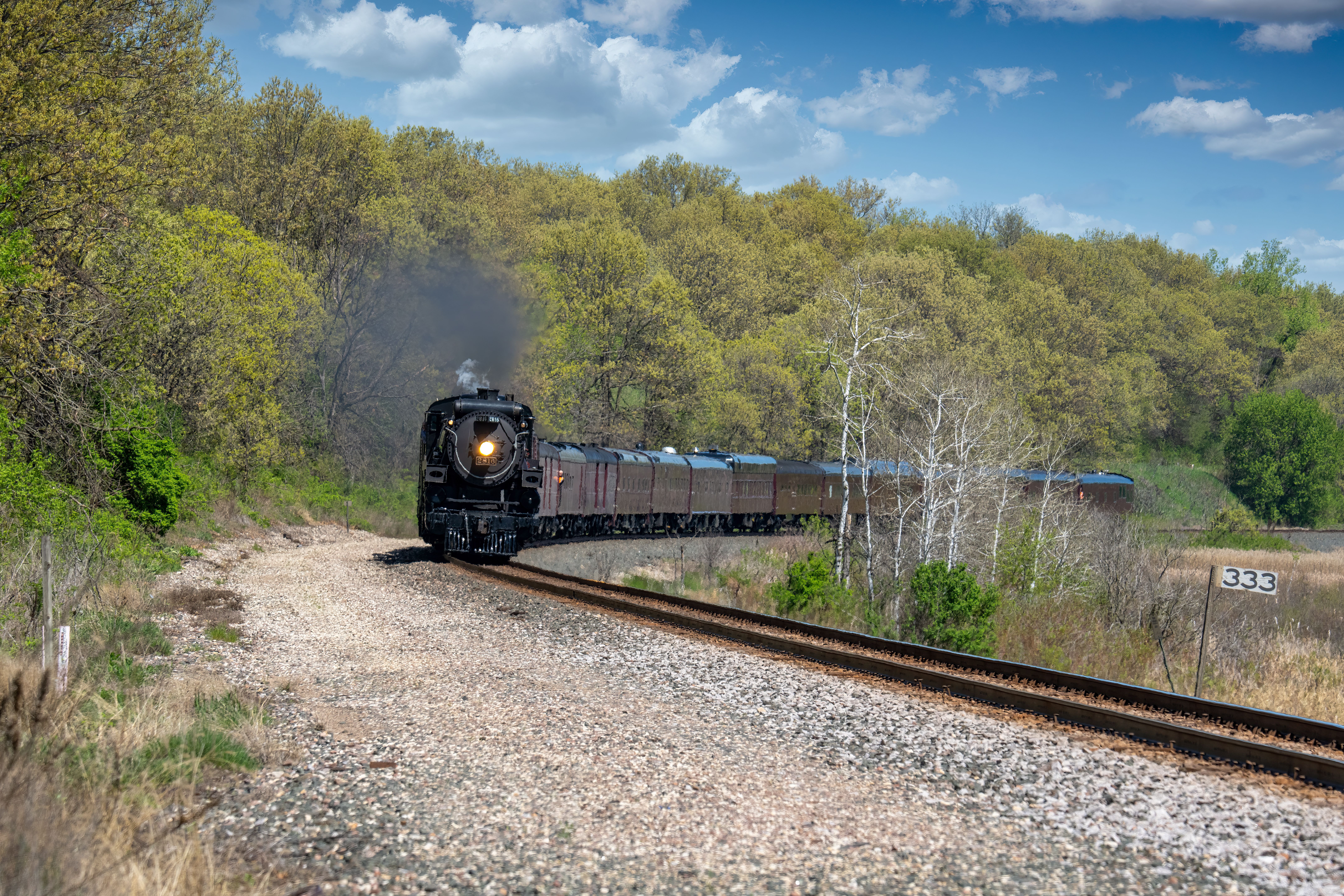 A vintage steam train travels through a rural forest landscape in Kellogg, MN, USA.