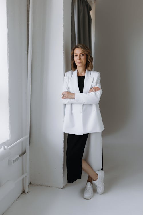 A woman in a white coat and black dress standing in front of a window