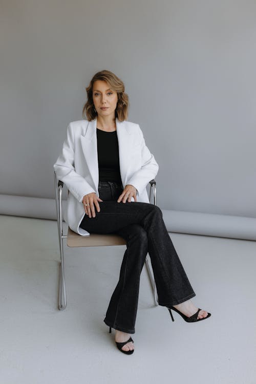 A woman in a white blazer and black pants sitting on a chair