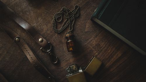 Free A rustic still life featuring a vintage vial necklace, lighter, and leather strap on a wooden table. Stock Photo