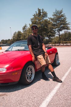 阳光明媚的停车场里，年轻人对着一辆红色敞篷车放松