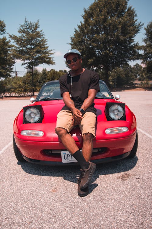 Photo of a Man Wearing Black Shirt Sitting on Red Car Hood