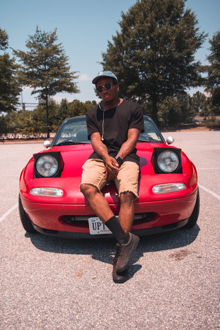 Photo Of A Man Wearing Black Shirt Sitting On Red Car Hood