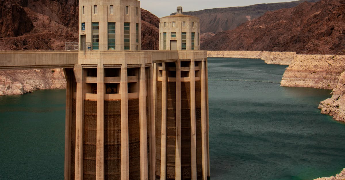 Photo by Cameron Rainey Scenic shot of Hoover Dam towers amidst rocky landscape and calm waters.