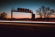 黄昏时分，高速公路的长镜头曝光引人注目，呈现出灯光小径和树木的剪影