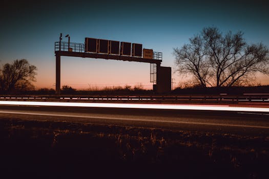 黄昏时分，高速公路的长镜头曝光引人注目，呈现出灯光小径和树木的剪影
