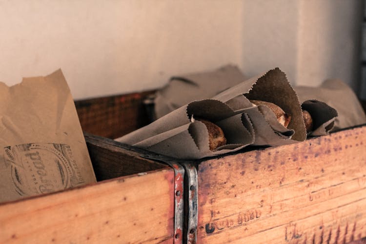 Photograph Of Food Packaged  In Grey Kraft Paper Bags Placed  In Brown Wooden Open Boxes