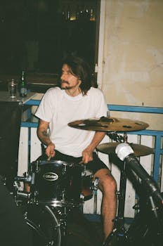 Drummer performing live on stage indoors with acoustic drum set.
